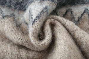 Macro shot of thick beige jacquard knit fabric with fluffy long fibers and grey patterns