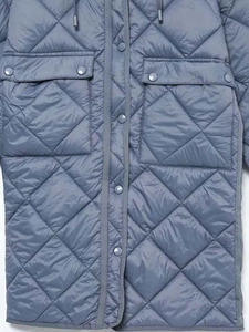 Dettaglio di un cappotto lungo trapuntato blu con cappuccio e bottoni a pressione