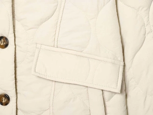 Detail of cream quilted jacket showing intricate stitching and tortoise shell buttons