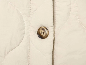 Macro detail of wave-quilted beige jacket fabric with a brown tortoiseshell button
