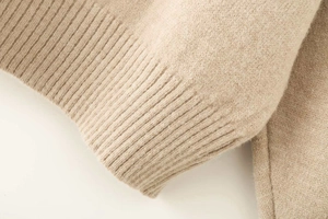Close-up of beige knit sweater showing soft wool blend texture and ribbed cuff detail