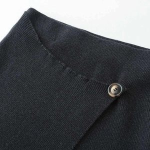 Minimalist black knit long skirt with asymmetrical hem and tortoiseshell button detail