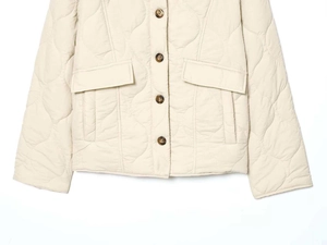 Detail of beige quilted jacket featuring wavy stitching and brown tortoiseshell buttons