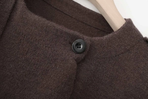 Detail of the knit texture and round black button on a dark brown asymmetrical cardigan