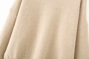 Detail of oatmeal knit sweater showing drop shoulder seams and ribbed hem texture