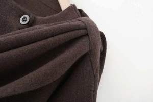 Detailed close-up of dark brown knitted poncho sweater showing shoulder seam and matte button