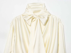 Nahaufnahme von elegantem Satinhemd in Creme mit großer Zierschleife und feinen Falten
