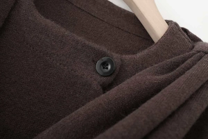 Detail of dark coffee knit sweater featuring a black button and layered pleat design