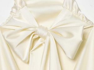 Makro-Detail einer eleganten cremeweißen Satinbluse mit großer dekorativer Schleife