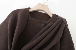 Detail of dark brown knit cape sweater featuring a round black button and soft draped pleats