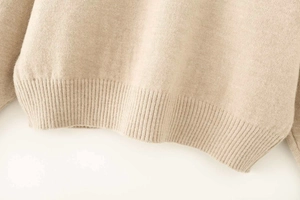 Close-up of ribbed hem on beige knit sweater showing fine texture and soft material