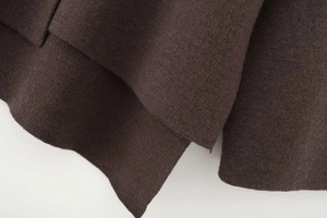 Detailed macro view of asymmetric hemline on thick dark brown knitted poncho sweater