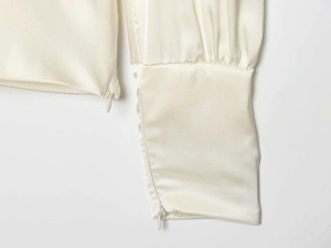 Detail der eleganten cremefarbenen Satinbluse mit unsichtbarem Reißverschluss und glattem Stoff