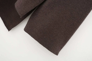 Close-up detail of dark coffee knitted wool fabric texture on asymmetrical cloak sweater