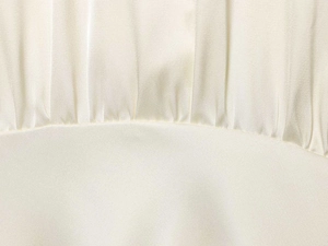 Makroaufnahme von elegantem cremefarbenem Satinstoff mit edler Plissee-Struktur und Fall