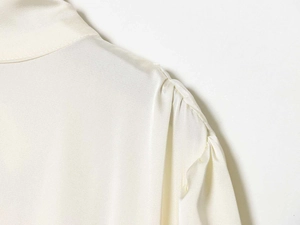 Detail der Schulterfalten und des cremeweißen Satinstoffs an der eleganten Damenbluse