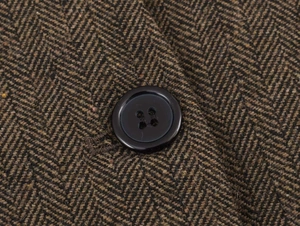 Macro detail of herringbone tweed texture and resin button on a casual blazer jacket