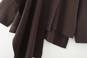 Detail view of the chocolate brown knit texture and asymmetric layering on the cape sweater