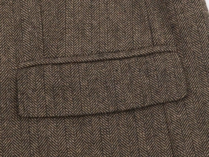 Close-up of herringbone texture and flap pocket detail on a brown wool blazer