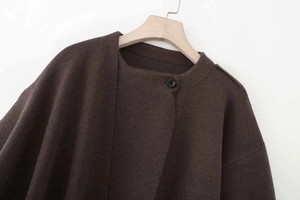 Detail of dark brown knit poncho with a single black button and soft wool texture