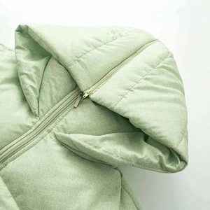 Détail d'une veste à capuche vert clair avec motif monogramme et fermeture à glissière
