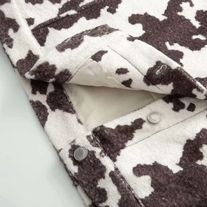 Detail of animal print jacket featuring cow pattern wool fabric and silver metal button