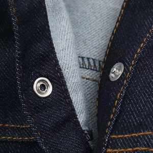 Dettaglio del tessuto denim blu scuro con cuciture a contrasto arancioni e bottone in metallo