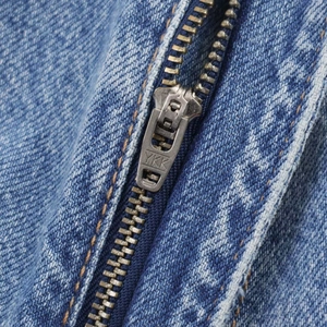 Détail macro de la fermeture éclair YKK en métal et surpiqûres sur denim bleu lavé