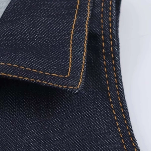 Dettaglio del tessuto denim blu scuro con cuciture a contrasto arancioni e texture