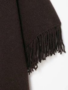 Close-up of dark brown knit poncho featuring detailed fringe trim and thick fabric texture
