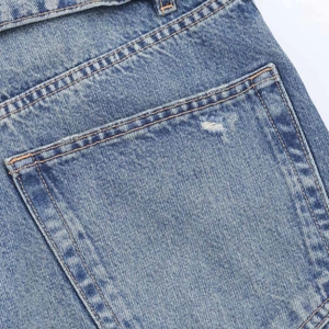 Détail macro du denim délavé bleu clair avec coutures orange et poche arrière usée