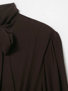 Dettaglio della camicetta in chiffon marrone scuro con colletto a fiocco e spalla a pieghe