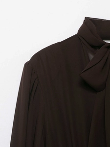 Dettaglio ravvicinato della camicetta di chiffon marrone scuro con fiocco e pieghe spalla