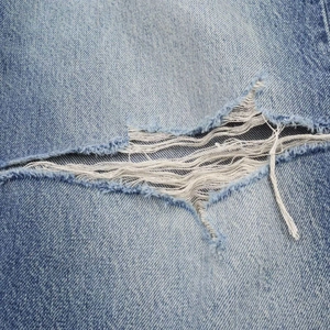 Détail macro d'un jean denim usé montrant des trous déchirés et des textures