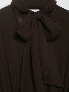 Dettaglio di un grande fiocco su un abito in chiffon marrone scuro con texture pregiata
