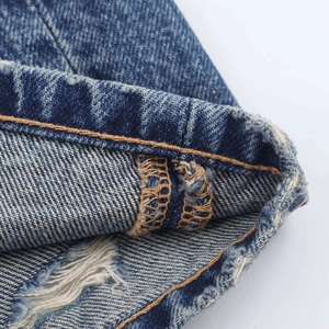 Détail macro de l'ourlet en denim bleu avec bords effilochés et doubles coutures jaunes