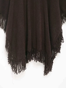 Close-up of deep brown knitted cape featuring intricate tassel fringe trim and warm texture