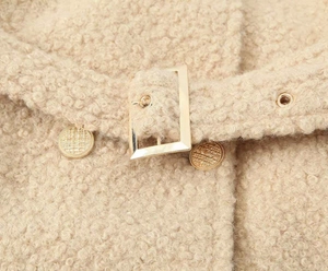 Detail of almond teddy coat waist featuring a golden buckle belt and textured buttons