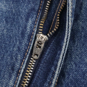 Détail d'une fermeture éclair en métal argenté YKK sur un tissu en denim bleu foncé robuste