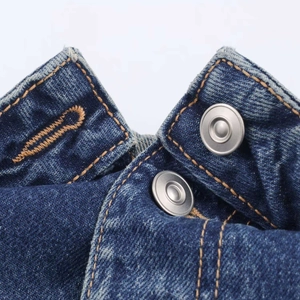 Détail du jean en denim bleu foncé avec deux boutons métalliques et coutures orange apparentes