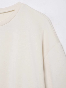 Gros plan sur le col rond côtelé et les coutures d'un t-shirt de couleur crème en coton