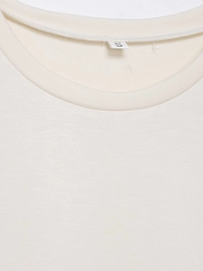 Détail du col rond et de l'étiquette de taille sur le t-shirt en maille crème