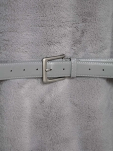 Dettaglio di un gilet in ecopelliccia grigia con cintura in similpelle e fibbia in metallo