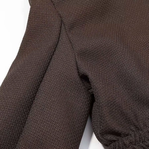 Detailed view of dark brown textured fabric with visible cuff stitching and heavy weave