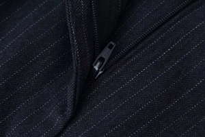 Close-up of black zipper detail on pinstripe herringbone trousers fabric texture