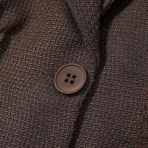 Close-up of brown textured tweed blazer fabric with matching matte four-hole button
