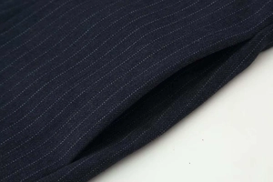 Close-up detail of dark blue pinstripe trousers fabric and high-quality pocket stitching