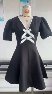 Détail du col en V avec bordure contrastée blanche et nœuds sur la mini robe noire
