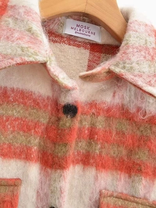 Dettaglio del colletto della giacca a quadri in peluche rosso e beige con etichetta