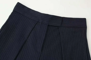 Macro detail of navy blue pinstripe wide-leg trousers showing waist pleats and fabric texture